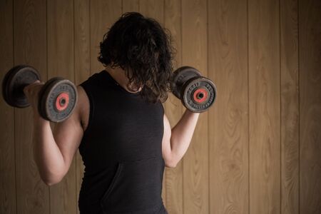 A guy exercising at home with dumbbells, stretching, shoulder exercises and boxing warm-upの写真素材