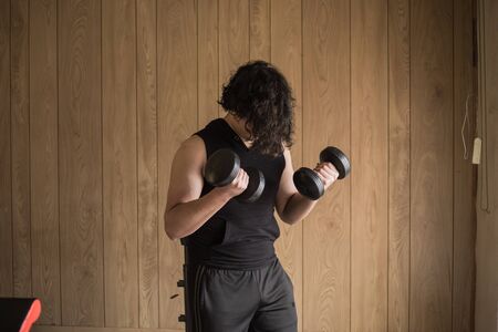 A guy exercising at home with dumbbells, stretching, shoulder exercises and boxing warm-upの写真素材