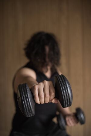 A guy exercising at home with dumbbells, stretching, shoulder exercises and boxing warm-upの写真素材