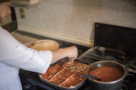 housewife cooking lasagna with vegetables in a white wooden kitchenの写真素材