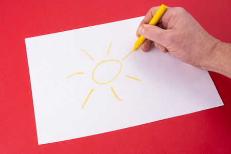 a sun drawn on a sheet of white paper with wax crayonsの写真素材