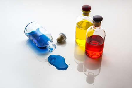 blue liquid spill by a small glass bottle on a white surfaceの写真素材