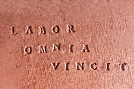 the phrase  âLabor Omnia Vincitâ written in Latin on a terracotta tabletの写真素材