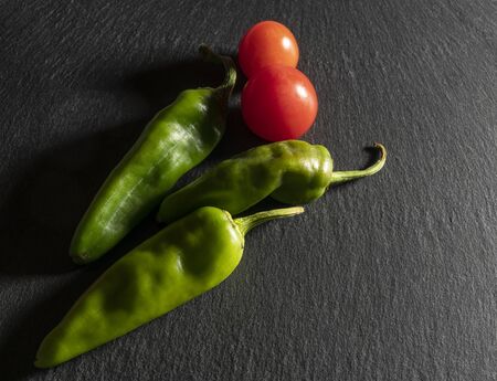 some tomatoes and two green peppers on a black stone saurfaceの写真素材