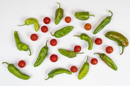 A composition of some green peppers and tomatoes on a white surface