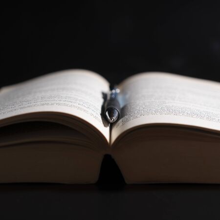 An open book in dim light with a pen on itの写真素材