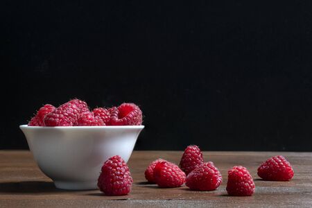 A white bowl with some fruits of  raspberries on a wooden surfaceの写真素材