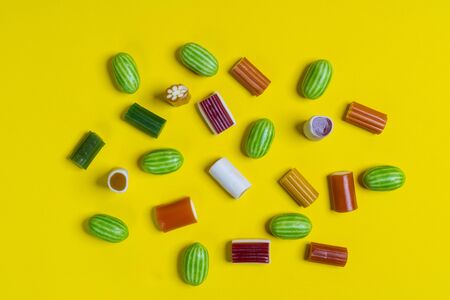 some colorful candies of various shapes on a yellow surfaceの写真素材