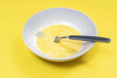 A beaten egg on the plate ready to be cooked on a yellow surfaceの写真素材