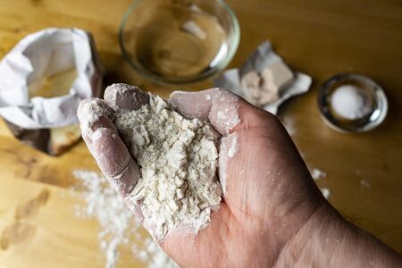 wheat flour in the hand with the ingredients for making bread on the table in the background