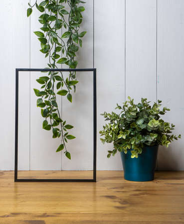 one blank black frame, an ivy and a lamp on the table with a white wood backgroundの写真素材