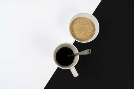 a cup of coffee and a bowl of sugar on a black and white surfaceの写真素材