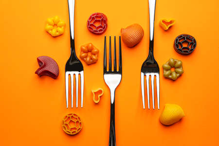 two forks with some types of colored pasta on a yellow surfaceの写真素材
