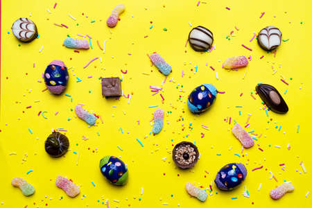 Multicolored sugar sprinkles, chocolates and sweets on a yellow surfaceの写真素材