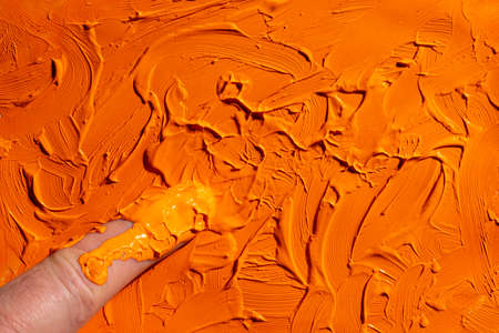 spread a patch of orange acrylic color with your fingerの写真素材