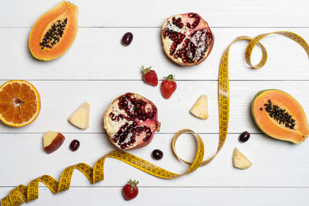 the concept for the diet: some fruits and a tape measure on a white wooden table