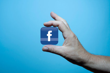 the Facebook symbol between the fingers of one hand with the blue background