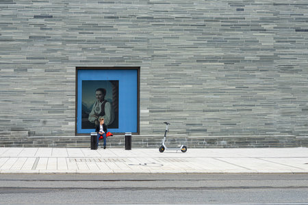 Oslo, Norway. September 2021. a boy sitting waiting with a reproduction of a painting behind him on a perimeter wall of the National Art Museum in the city centerのeditorial素材