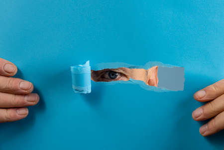the eye of a man looking through the tear in a sheet of paperの写真素材