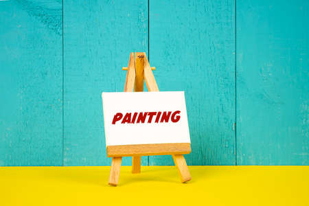 a wooden easel with the word Painting painted on a white canvasの写真素材
