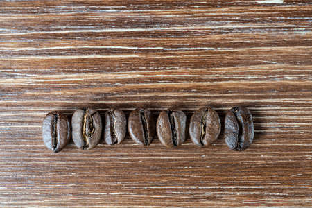 detail of a row of roasted coffee beans on a wooden surfaceの写真素材