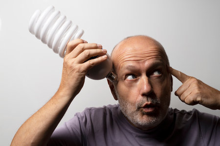 the concept of idea with a huge low consumption electronic light bulb in the hand of a thinking manの写真素材