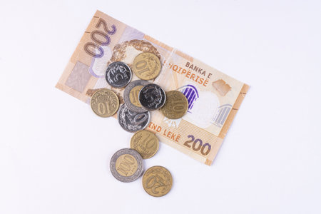 some coins and a Lek banknote of Albanian currency on a white surface