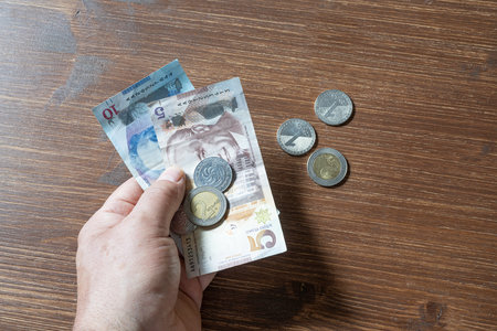 some Georgian Lari banknotes and coins in the hand with some coins on the table in the background