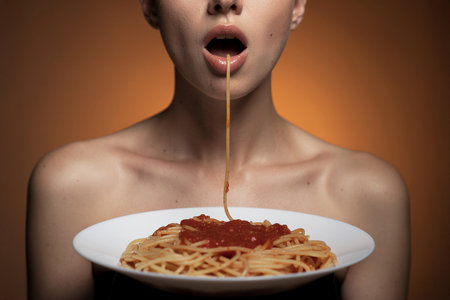 AI generated image. a woman in front of a plate of spaghetti with a string of bacon hanging from her mouthの素材