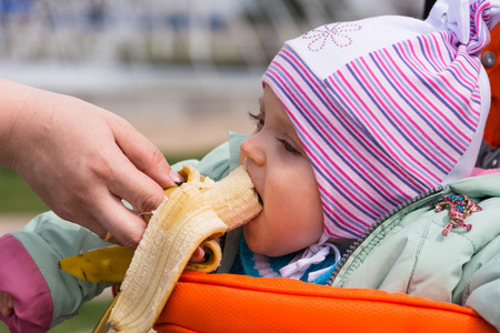 Picture of a little girl sitting in a wheelchair  Mother feeds her a banana  In the picture, only the hand of Moms with fruit の写真素材