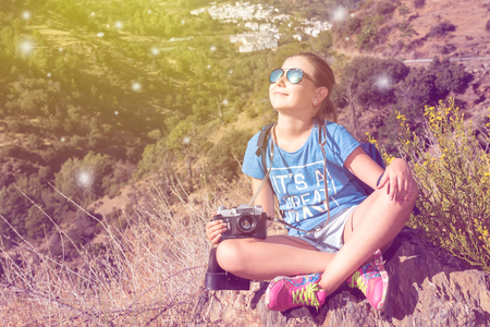 the little beautiful girl with the camera has been photographed on walk in mountainsの写真素材