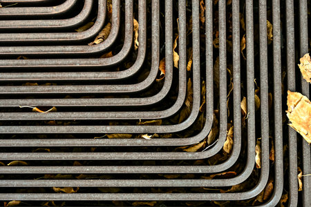 Iron tree grate with geometric design, covered by dry autumn leaves, combining urban structure with natural seasonal detailの写真素材