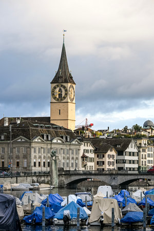 Scenic view of Limmat river in Zurich with boats, reflections, and St. Peter Church under a colourful morning skyの写真素材