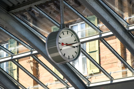 Swiss railway station clock with its distinctive minimalist design and red second hand, hanging under a glass roof structure. A symbol of precision and punctuality in Swiss train stationsの写真素材
