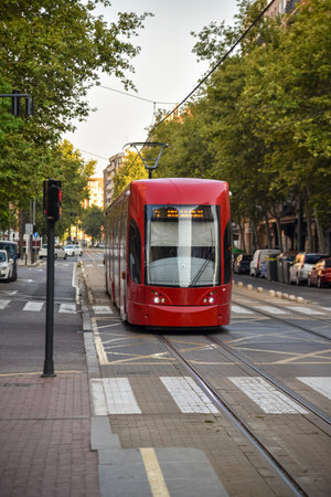 lonely tram on a quiet Valencia street on an early summer morning, with tram tracks, trees, parked cars, and soft golden lightの写真素材