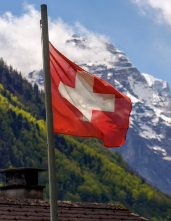 Swiss flag waving in the wind with the Glarus Alps in the background, combining national symbol and mountain landscapeの写真素材