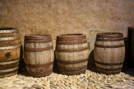 Row of old wooden barrels against a rustic wall on a cobblestone floor. Traditional handcrafted casks once used for storing wine, beer, or other goodsの写真素材