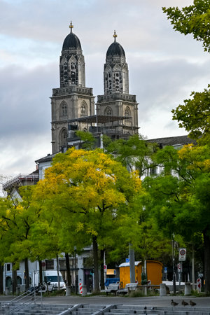 View of GrossmÃ¼nster Church towers in ZÃ¼rich, Switzerland, rising above autumn trees under a cloudy morning skyの写真素材