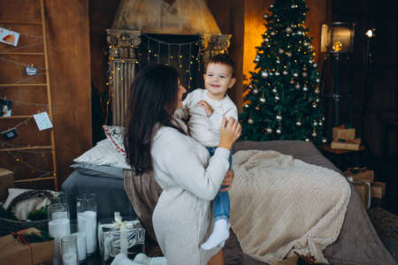beautiful brown-haired mom and lovely boy son sitting on the floor hugging and playing against the background of the Christmas treeの写真素材