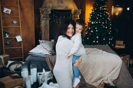 beautiful brown-haired mom and lovely boy son sitting on the floor hugging and playing against the background of the Christmas treeの写真素材