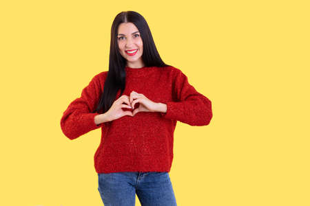 Close up photo beautiful amazing her she lady arm friendly show healthy heart shape figure form wearing red knitted sweater clothes outfit isolated yellow bright backgroundの写真素材