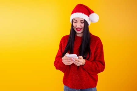 Young beautiful girl in a red Santa hat holds a phone in his hands. Christmas discount content.の写真素材