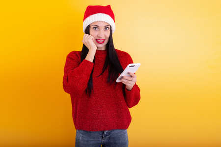 Young beautiful girl in a red Santa hat holds a phone in his hands. Christmas discount contentの写真素材