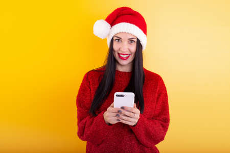 Young beautiful girl in a red Santa hat holds a phone in his hands. Christmas discount contentの写真素材