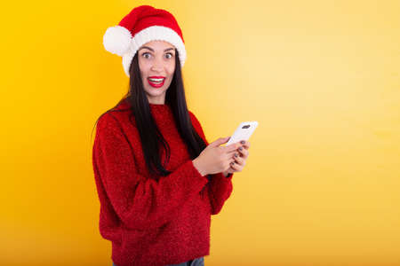 Young beautiful girl in a red Santa hat holds a phone in his hands. Christmas discount contentの写真素材