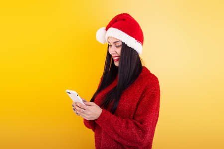 Young beautiful girl in a red Santa hat holds a phone in his hands. Christmas discount content.の写真素材