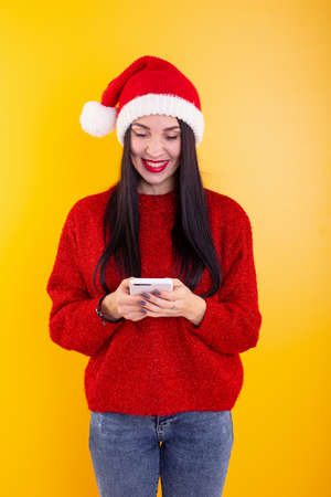 Young beautiful girl in a red Santa hat holds a phone in his hands. Christmas discount content.の写真素材