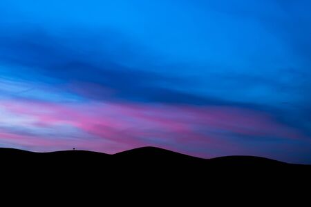 Lonely tree on the silhouette of the mountains with blue sky and pink clouds