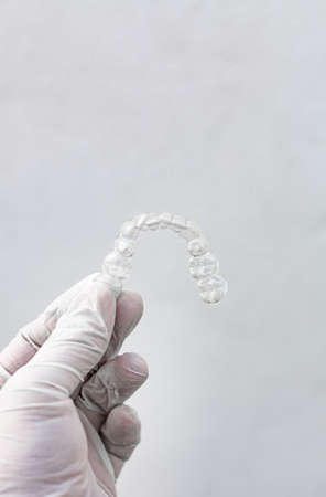 Invisible dental braces on white background held by a hand with hygienic glove