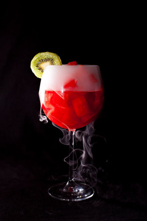 Refreshing cocktail of watermelon chunks with kiwi slice and dry ice vapor on dark backgroundの写真素材